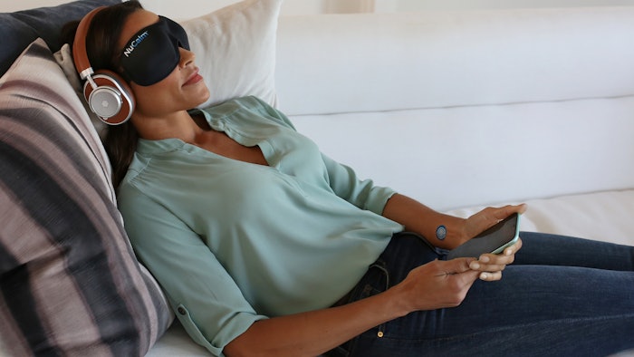 A woman resting on a couch while using headphones and an eye mask